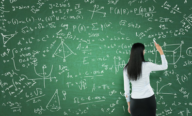 Rear view of a thoughtful woman who is writing math calculations on green chalk board.