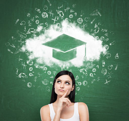 Business woman looking at the cloud with graduation hat over the head. Green chalk board as a background.