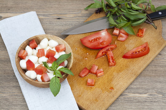 Sliced tomatoes, basil and mozzarella cheese on a wooden plate, selective focus