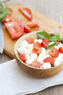 Sliced tomatoes, basil and mozzarella cheese on a wooden plate, selective focus