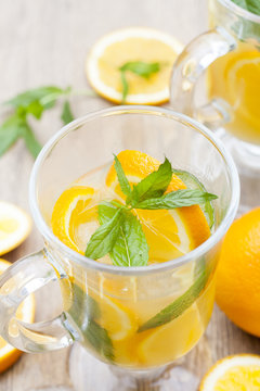 Orange fresh drinks with ice and mint on wooden table, selective focus