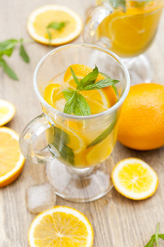 Orange fresh drinks with ice and mint on wooden table, selective focus