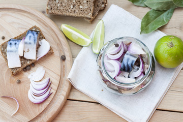 Slices of marinated mackerel with onion in a jar, lime, laurel and bread on wooden board
