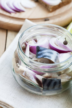Slices of marinated mackerel with onion in a jar, lime, laurel and bread on wooden board