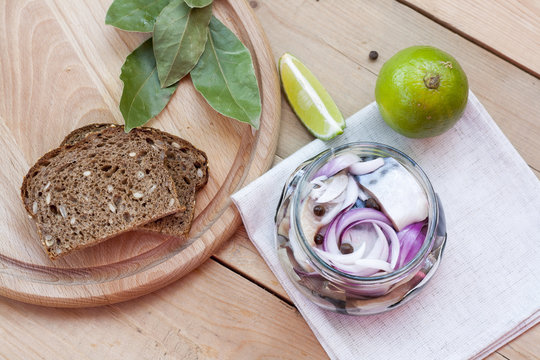 Slices of marinated mackerel with onion in a jar, lime, laurel and bread on wooden board
