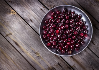 Cherry in metal bowl on old wooden background.