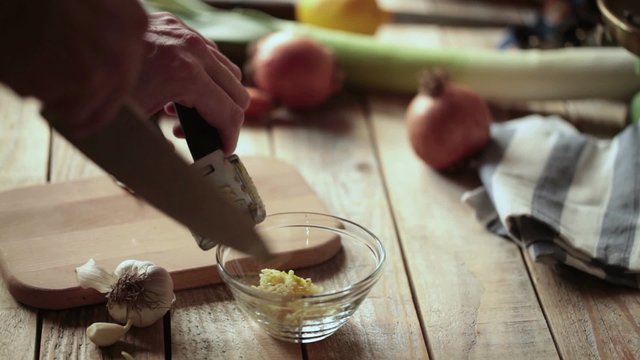 Chef squeezing garlic cloves using garlic press; close up; 