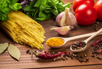 Raw pasta, vegetables, basil and spices on the wood table