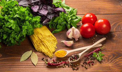 Raw pasta, vegetables, basil and spices on the wood table