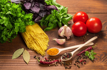 Raw pasta, vegetables, basil and spices on the wood table
