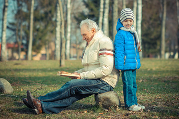Fototapeta premium Grandfather and grandson reading a book outdoors