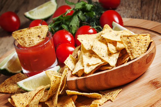Nachos in wooden bowl with sauce, tomatoes and lime, selective f