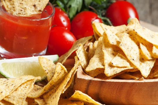 Nachos in wooden bowl with sauce, tomatoes and lime, selective f