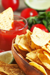 Nachos in wooden bowl with sauce, tomatoes and lime, selective f