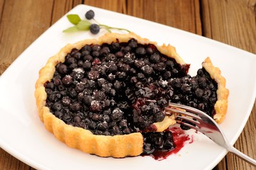 Juicy blueberry tart cut in square white plate with fork and wil