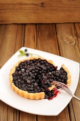 Homemade blueberry tart cut in square white plate with fork and