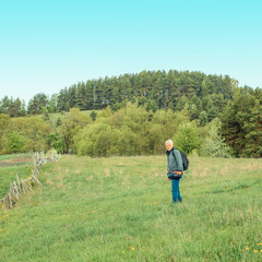 Naklejka na ściany i meble Elderly man travels in wildlife. Portrait of the gray-haired traveler in background of the landscape. Old photographer enjoys traveling and photography