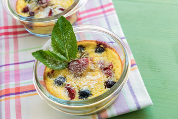 French clafoutis with blueberries and strawberries in ramekins on napkin and  turquoise wooden background