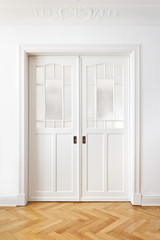 Obraz premium White old double sliding or pocket doors with textured glass in an old building with crown moldings.