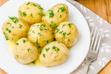 Traditional Ukrainian food boiled new potatoes with butter and dill on wooden table