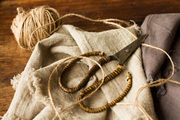 scissors lying on linen fabric with a rope on a wooden backgroun