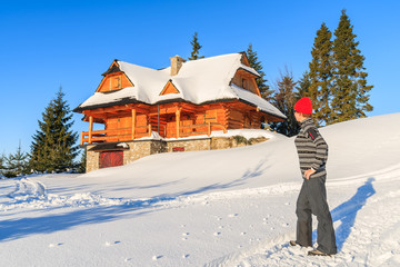 Young woman tourist standing in fresh snow in front of a mountain hut in Gorce Mountains in winter season, Poland