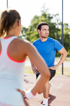 Young athletic man and woman stretching outdoors on a hot summer