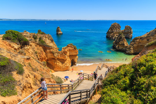 Fototapeta Unidentified young woman tourist taking photo of beautiful beach Praia do Camilo, Portugal