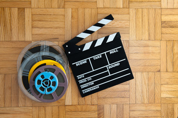 Movie clapper board and film reel on wooden floor
