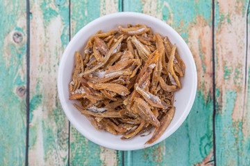 Deep fried anchovies in white bowl over rustic wooden background