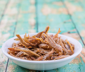Deep fried anchovies in white bowl over rustic wooden background