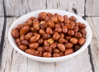 Deep fried peanuts in white bowl over rustic wooden background