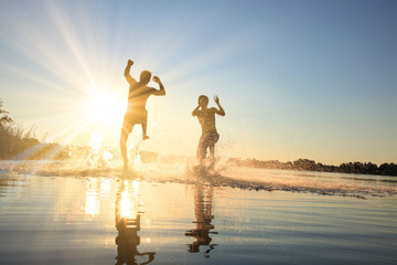 Glückliche junge Menschen laufen und springen am See beim Sonnenuntergang