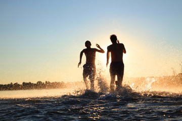 Glückliche junge Menschen laufen und springen am See beim Sonnenuntergang