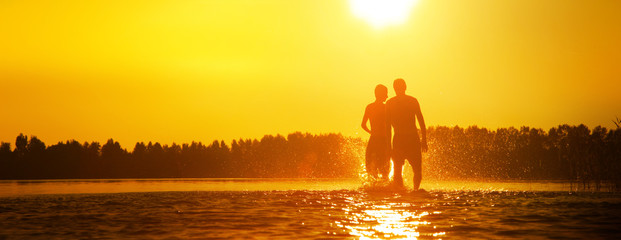 Glückliche junge Menschen laufen und springen am See beim Sonnenuntergang