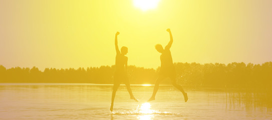 Glückliche junge Menschen laufen und springen am See beim Sonnenuntergang