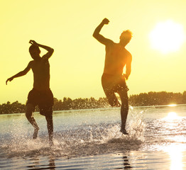 Glückliche junge Menschen laufen und springen am See beim Sonnenuntergang