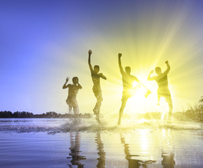 Glückliche junge Menschen laufen und springen am See beim Sonnenuntergang