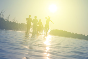 Glückliche junge Menschen laufen und springen am See beim Sonnenuntergang