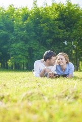 Naklejka na ściany i meble Young Caucasian Couple in love Outdoors Lying on Grass and Havin