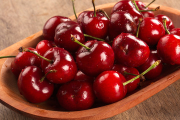 A wooden pot full of cherries over a wooden surface