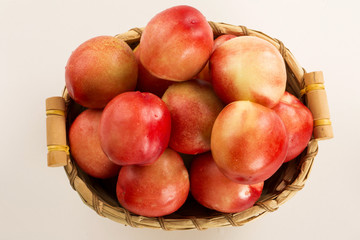 Some peaches in a basket over a wooden surface on a green and na
