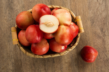 Some peaches in a basket over a wooden surface on a green and na