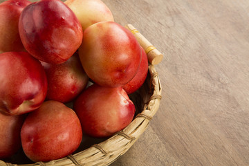 Some peaches in a basket over a wooden surface on a green and na