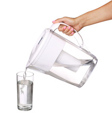 hand holding water filter jug and pouring water into a glass iso
