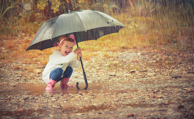 happy baby girl with an umbrella in the rain playing on nature