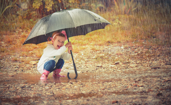 happy baby girl with an umbrella in the rain playing on nature