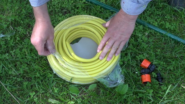 two hands rolling out new yellow water hose in meadow
