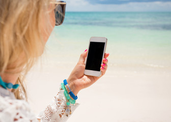 Woman holding smartphone in hand on the beach