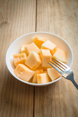 Cantaloupe in white dish with fork on wood background